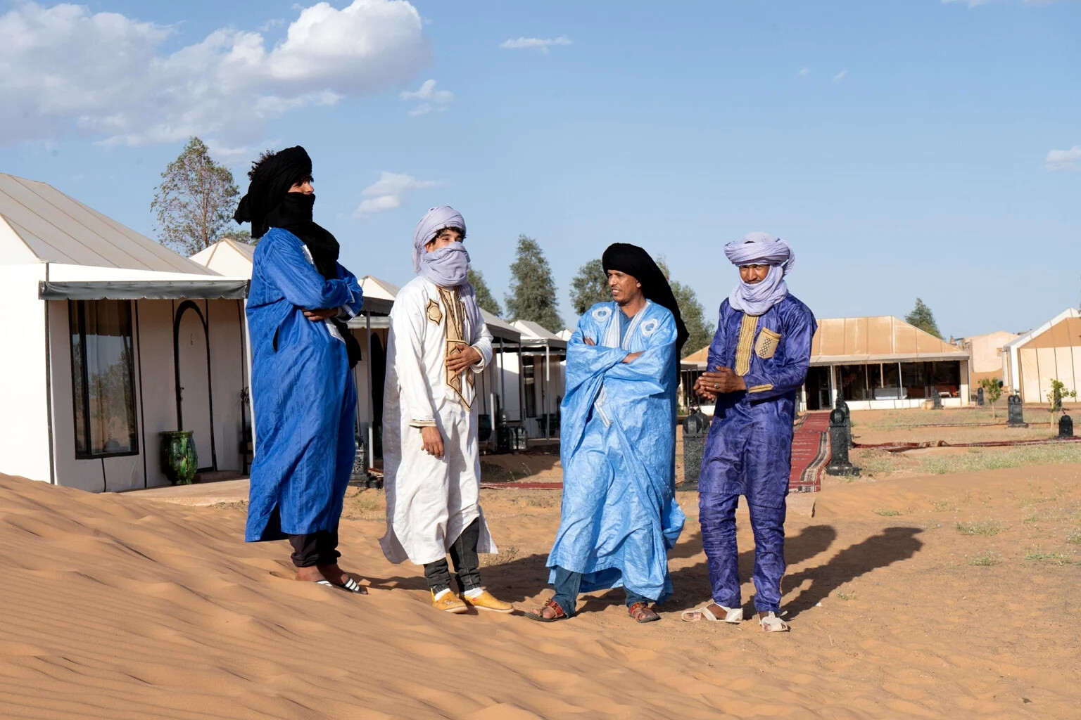 Four members of the camp team in blue and white desert robes standing on the sand beside the tents