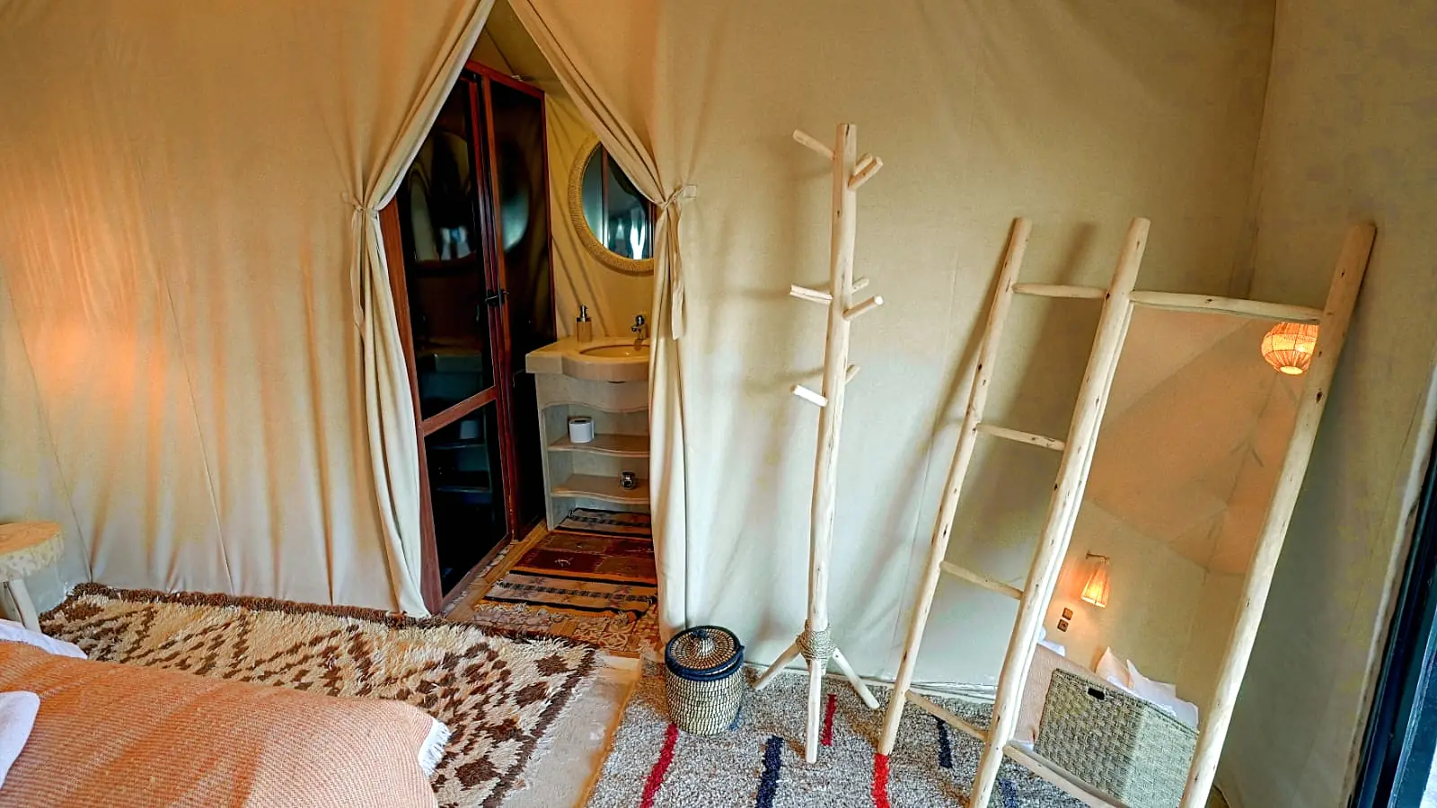 Corner of a tent showing the bed and the curtained entrance to the private ensuite bathroom with stone basin