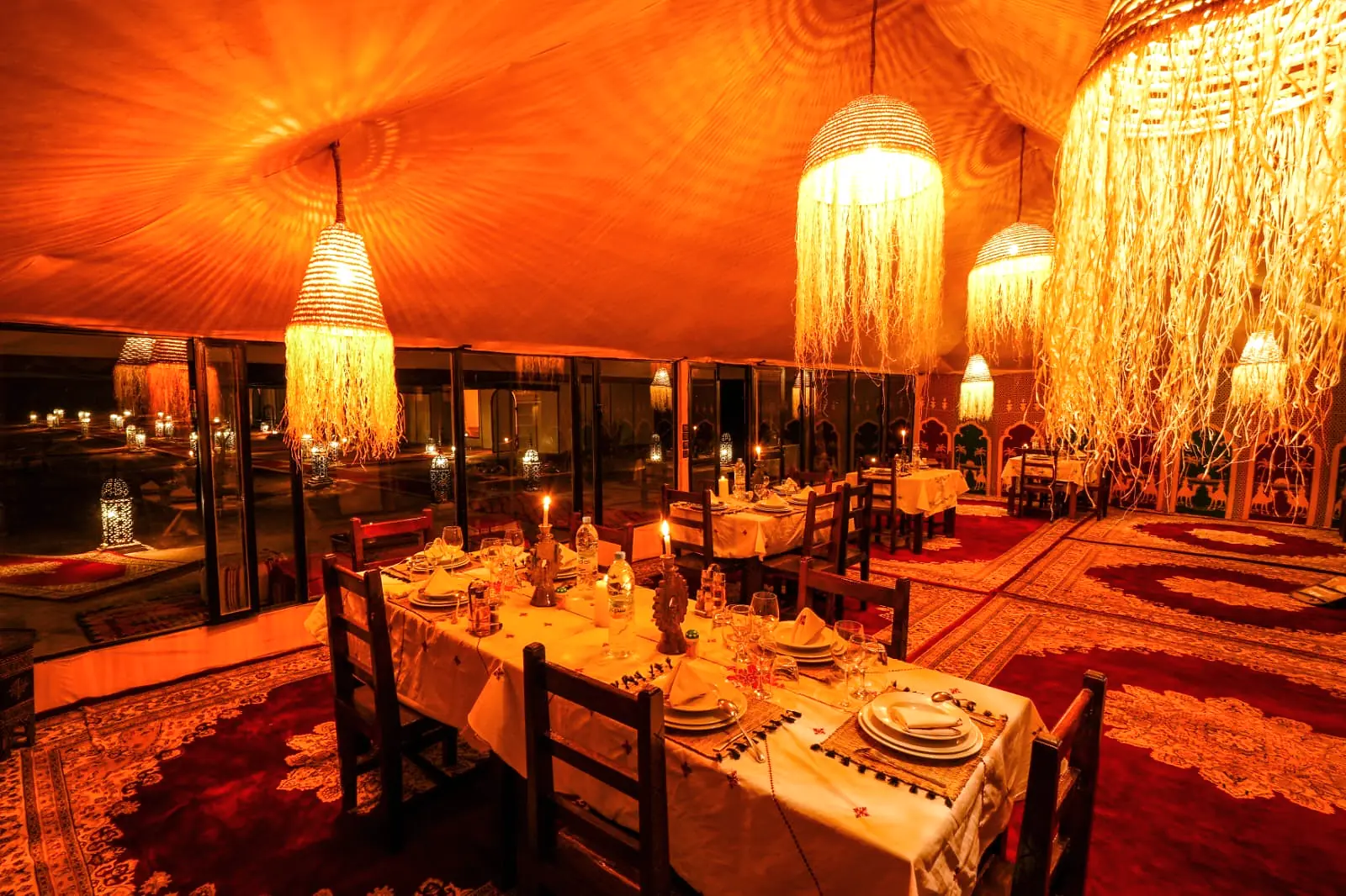 Wide interior of the dining pavilion with several set tables and traditional Moroccan rugs