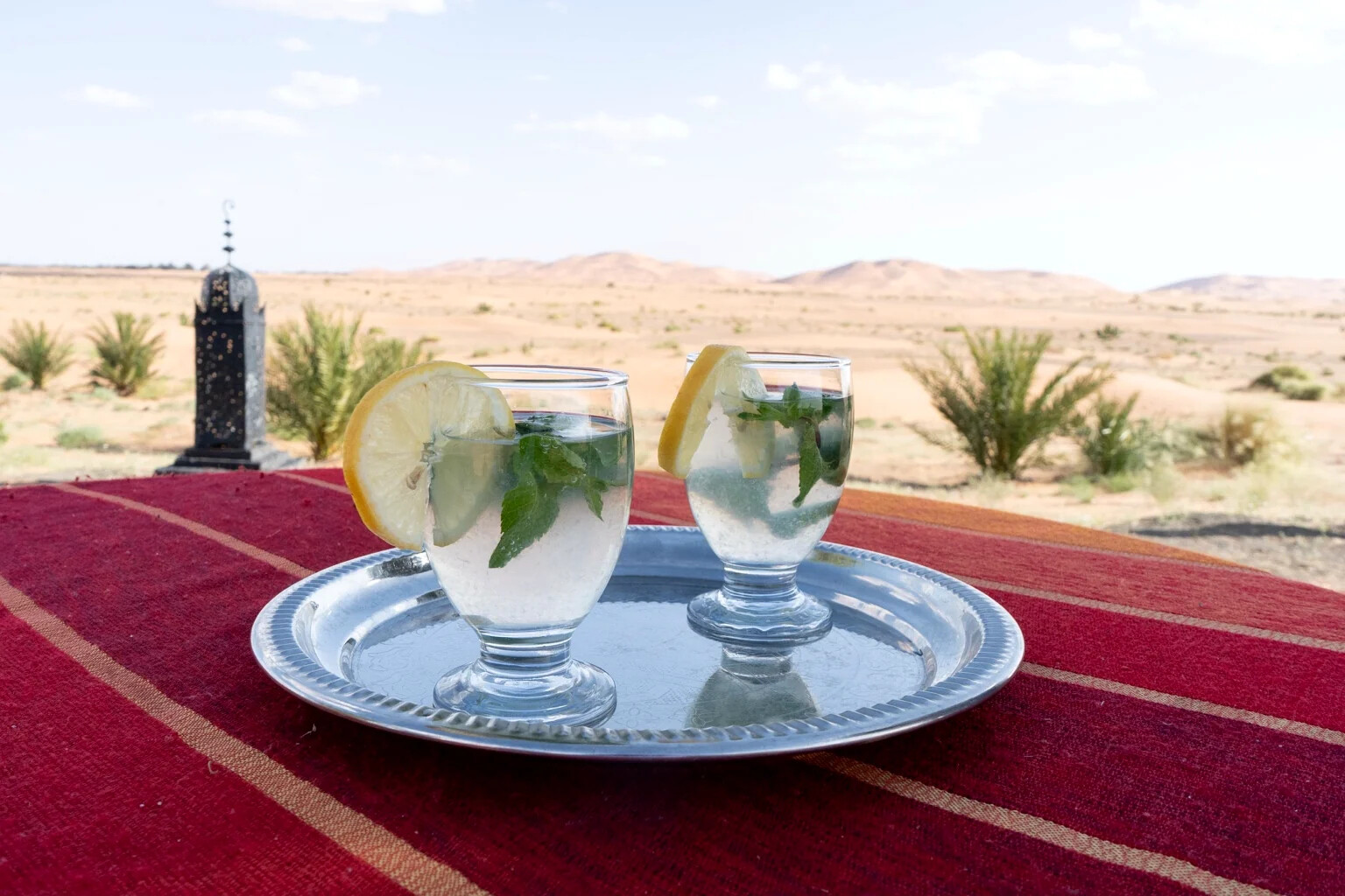Two welcome drinks with lemon and mint on a silver tray, set on a red rug facing the desert