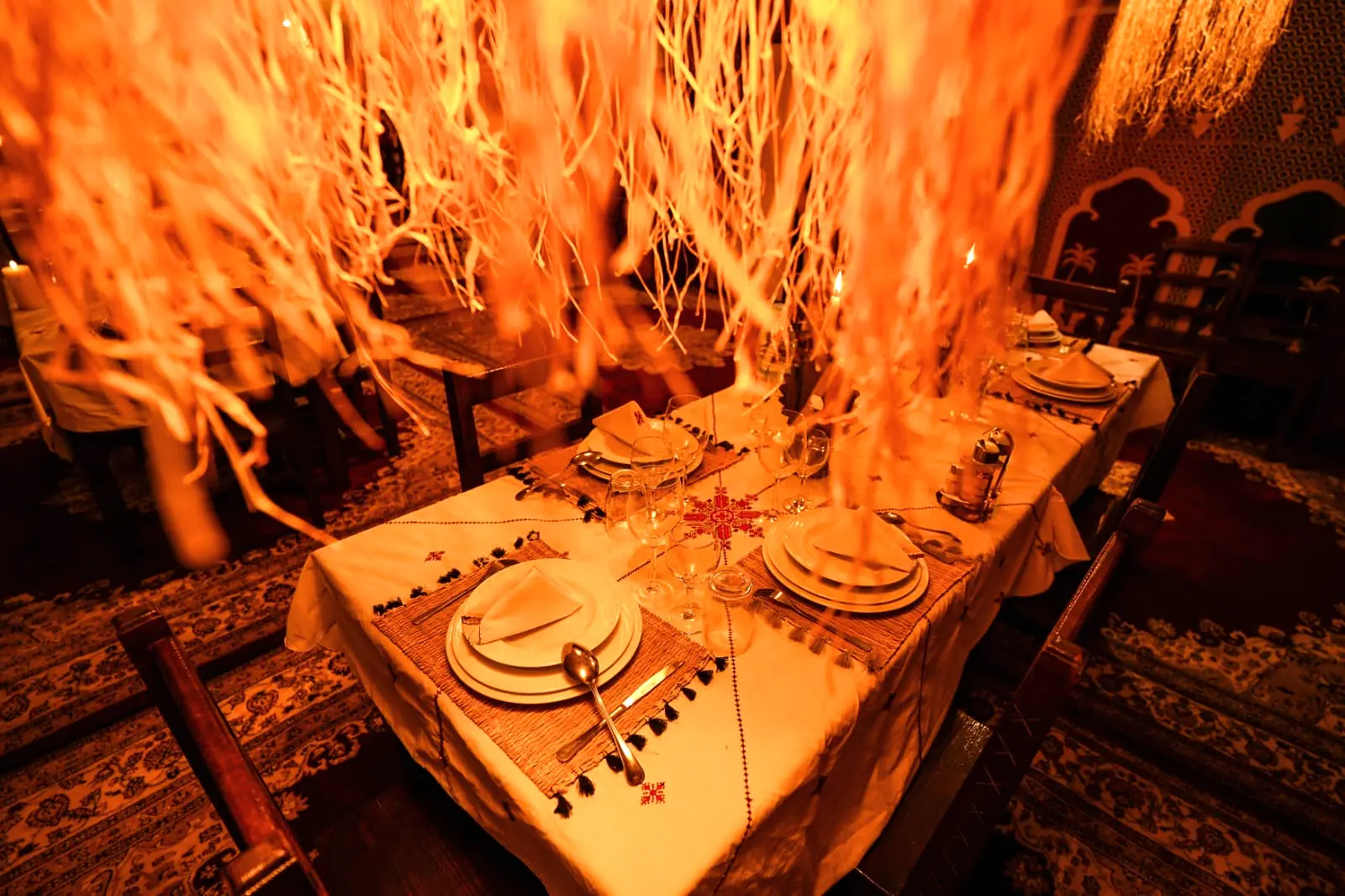 Dining table dressed with white linen and red accents under warm lamplight for a celebration dinner