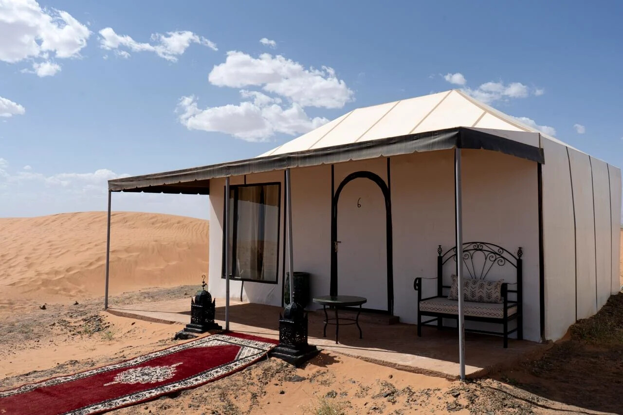 Exterior of a private desert tent with a red carpet entrance and a small shaded seating area