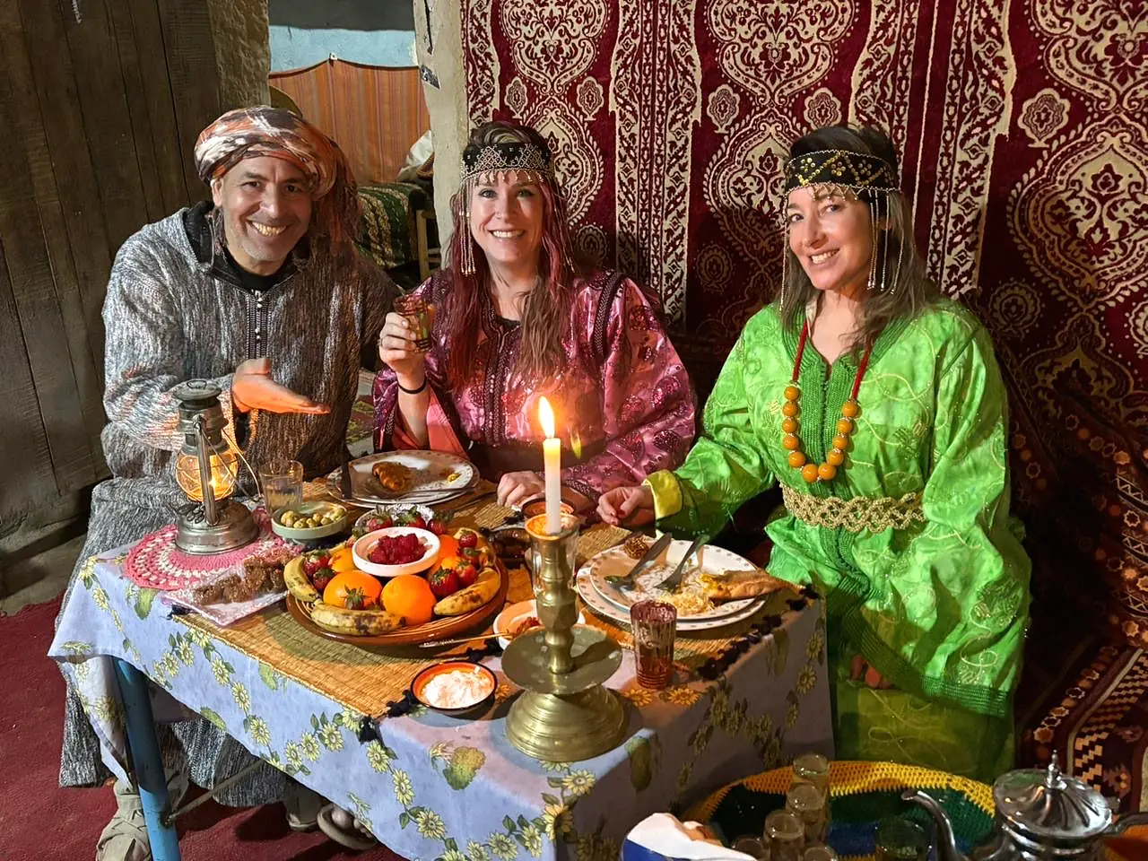 Mohamed sharing Medfouna, the local Berber pizza, with two guests at a family table in the desert