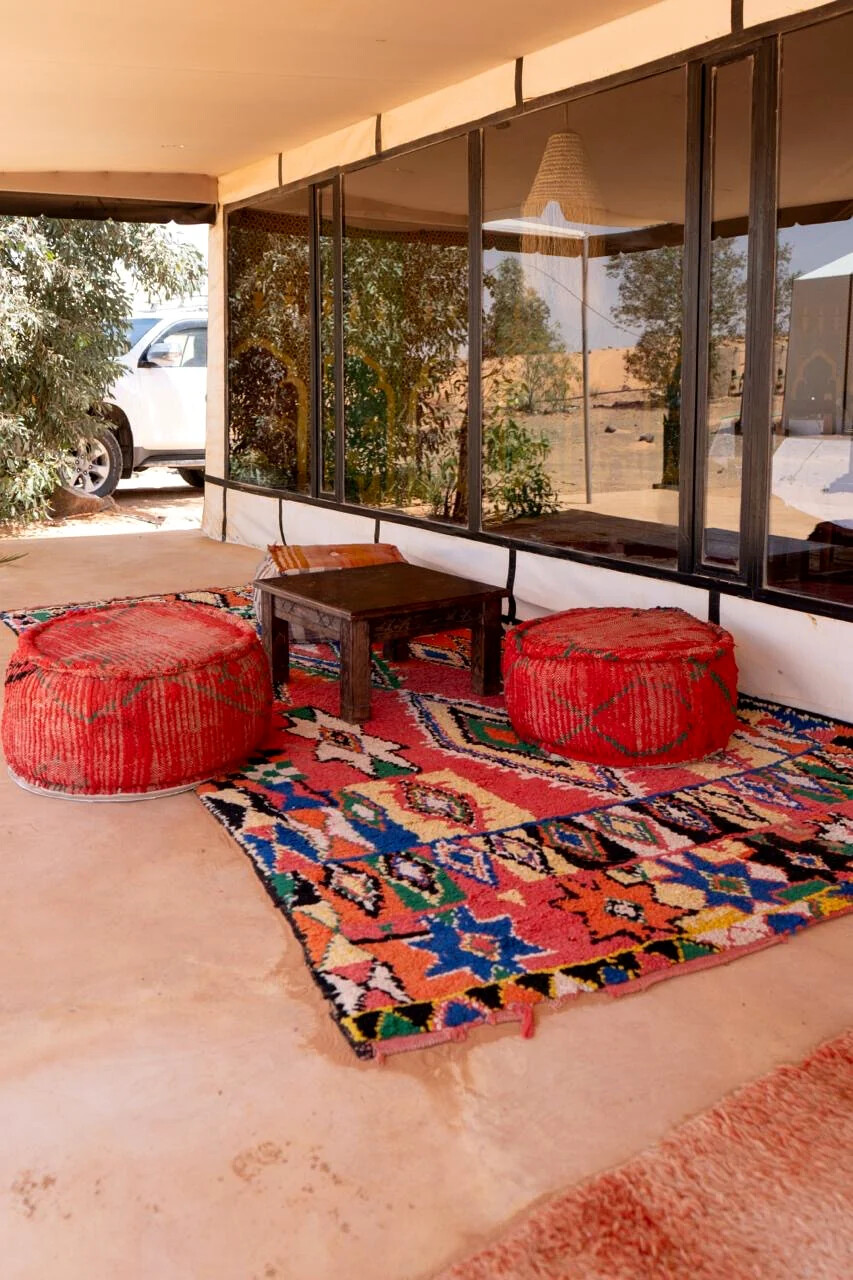 Outdoor lounge area laid with colourful Moroccan rugs and floor cushions on the sand