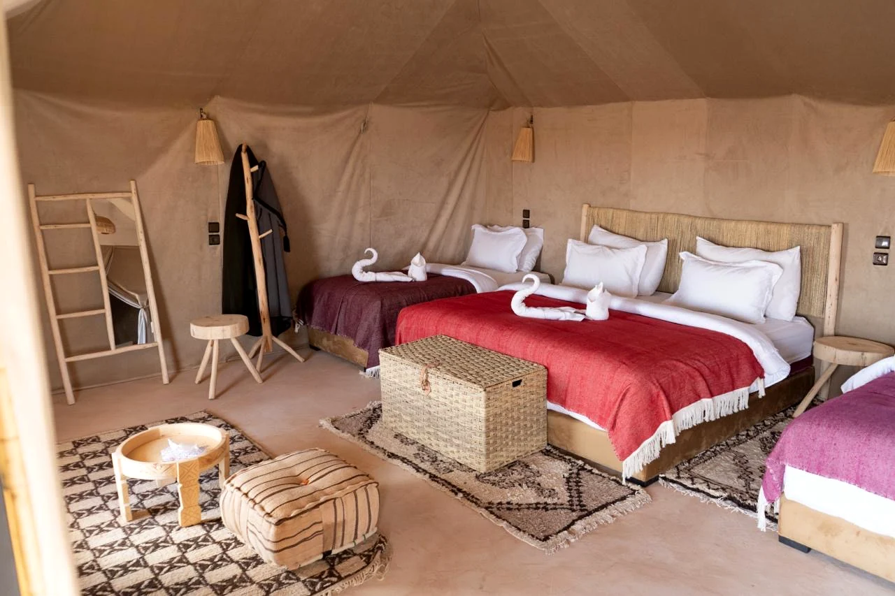 Interior of a large family tent with three beds, woven rugs, wooden furniture and warm sand-toned canvas walls