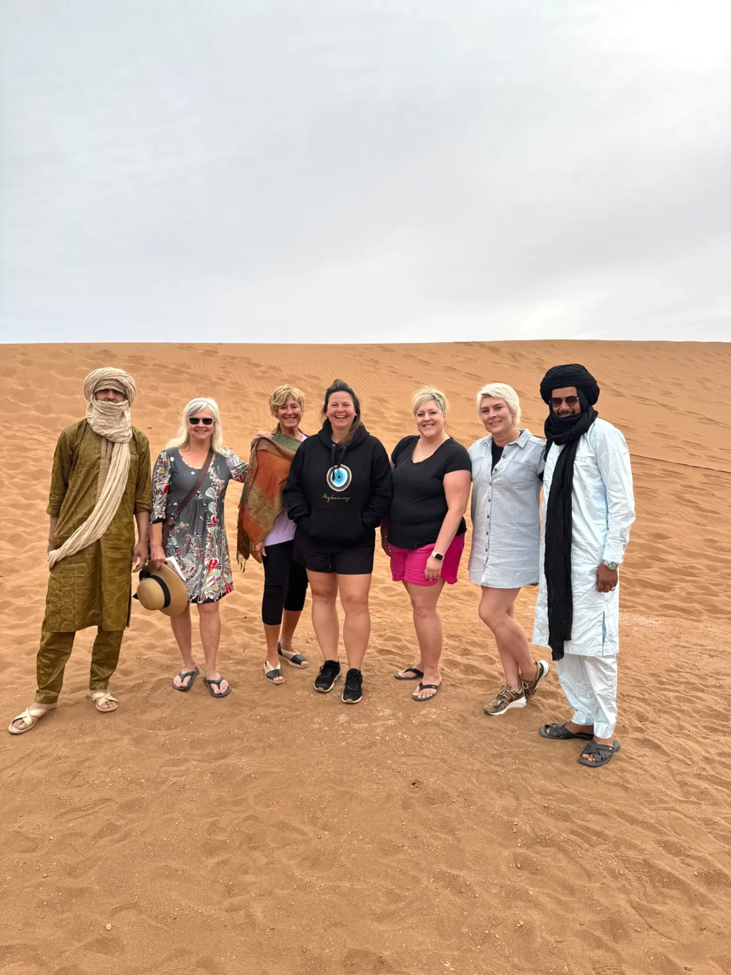 Oualid and Ali standing with a group of guests on the dunes of Erg Chebbi near Merzouga