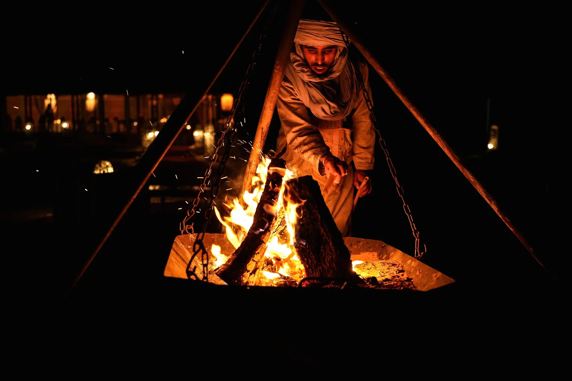 A host in traditional Saharan dress tending the open campfire at Arabian Nights Desert Camp at night
