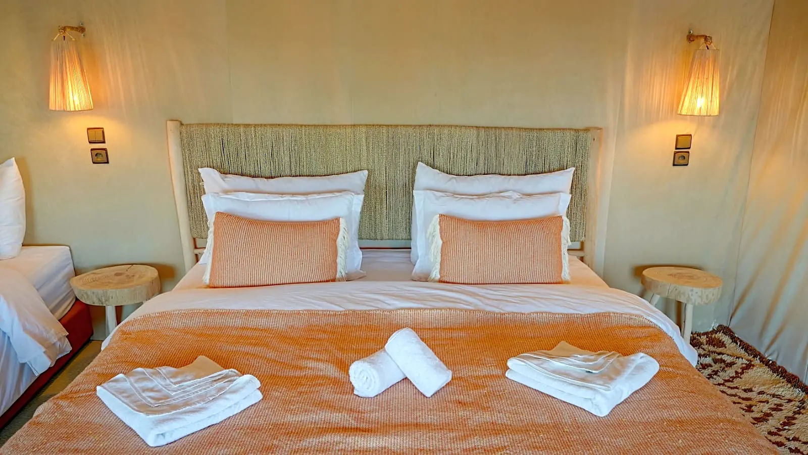 Calm deluxe tent interior with a large bed, orange throw and warm bedside lamps