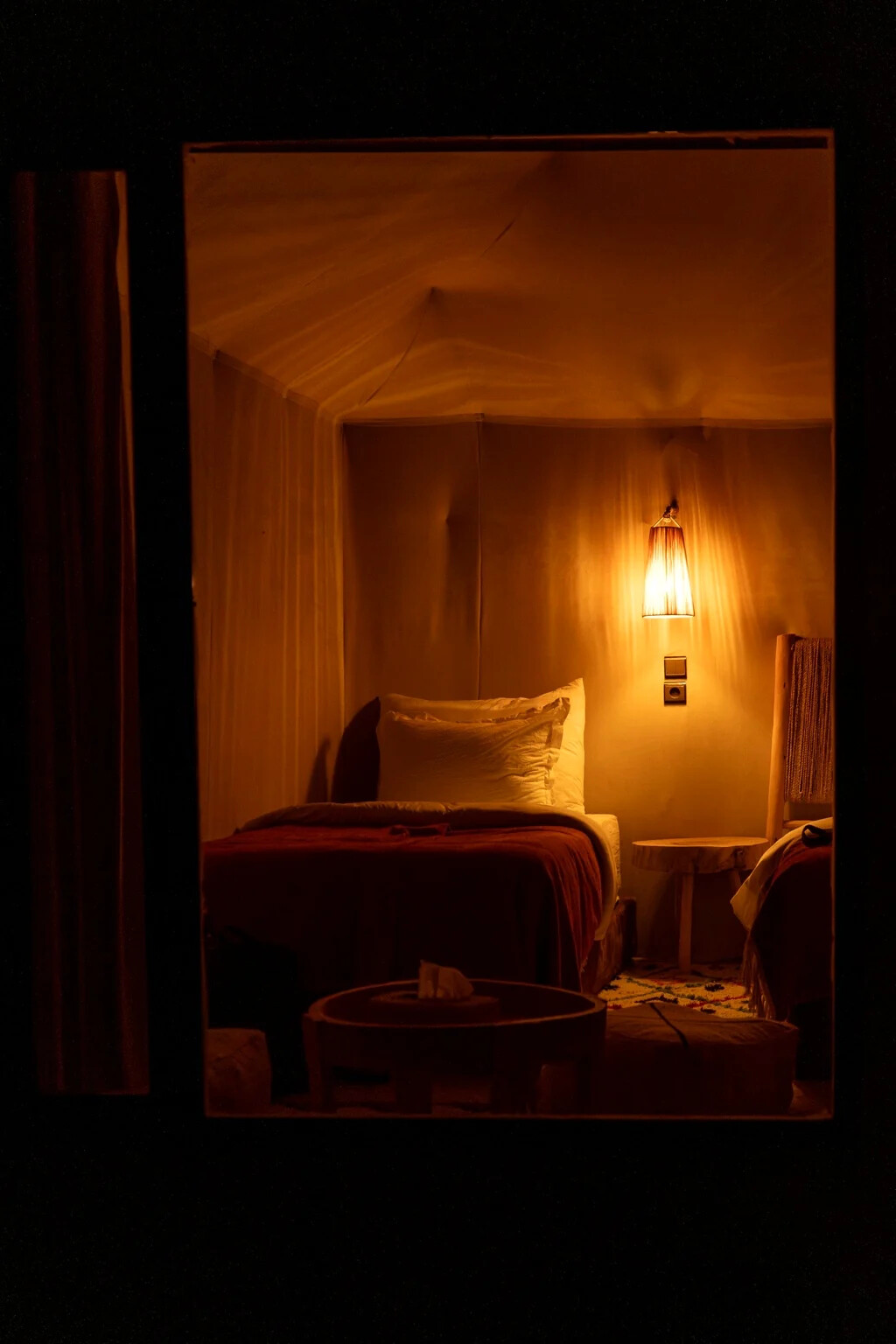 Warmly lit tent interior at night with a made bed and a glowing bedside lamp