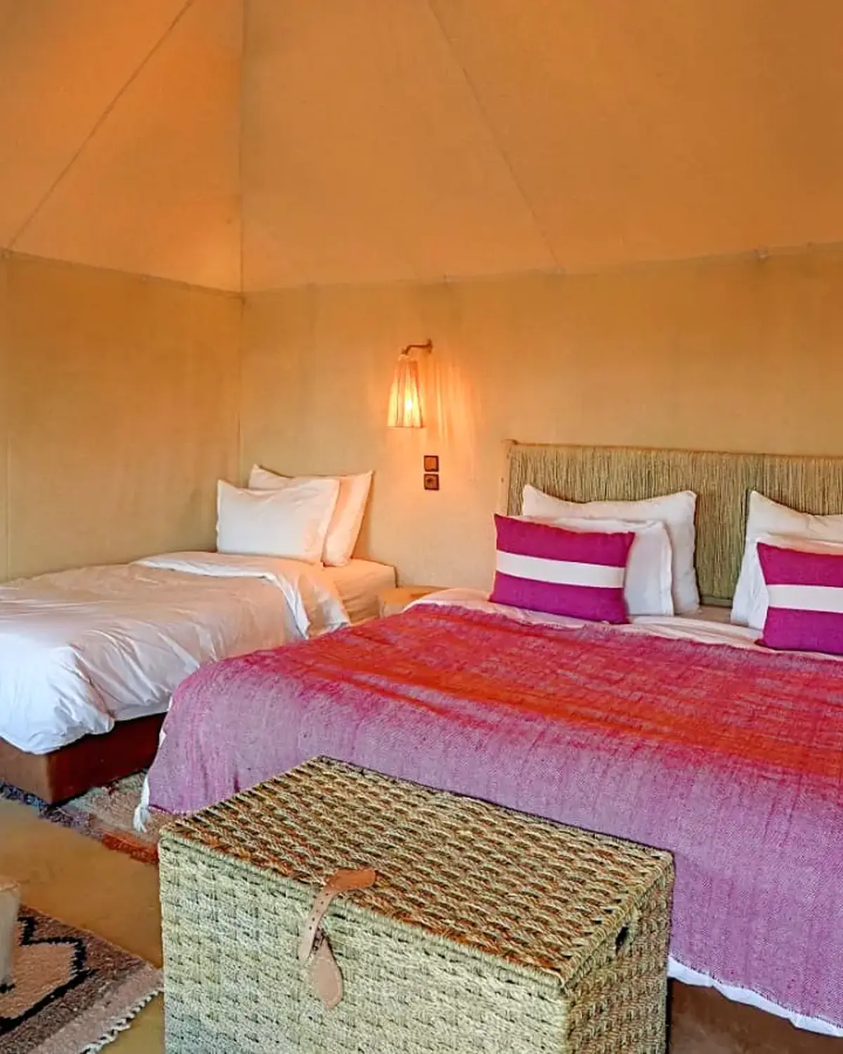 Interior of a deluxe tent with a large bed dressed in pink and orange Moroccan blankets and a single bed alongside