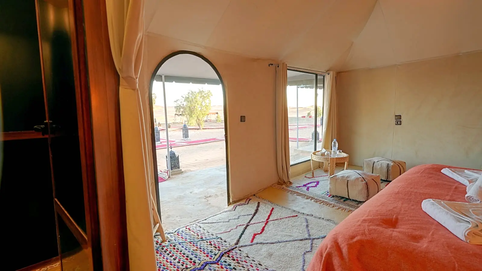 Tent interior with an arched doorway and large glazed window opening onto the desert and camp paths