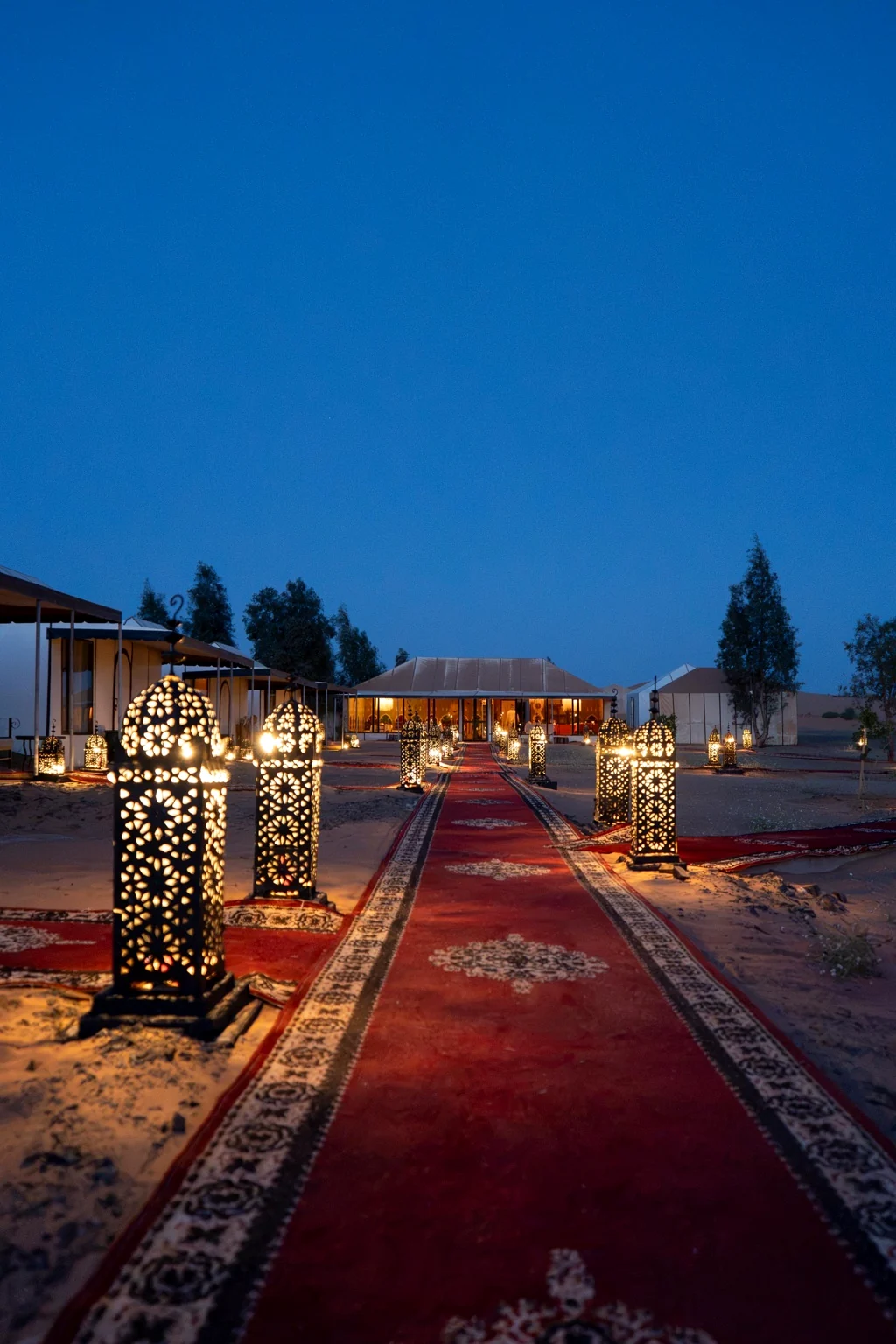 Ornate Moroccan lanterns lining the red carpet walkway towards the main dining tent at dusk
