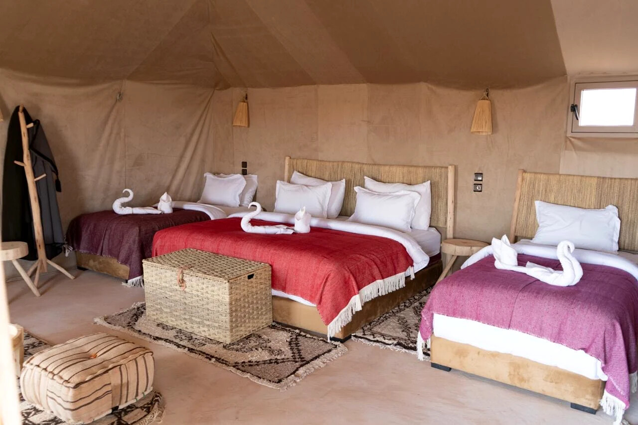Wide interior of a family tent with several beds dressed in red and purple Moroccan blankets