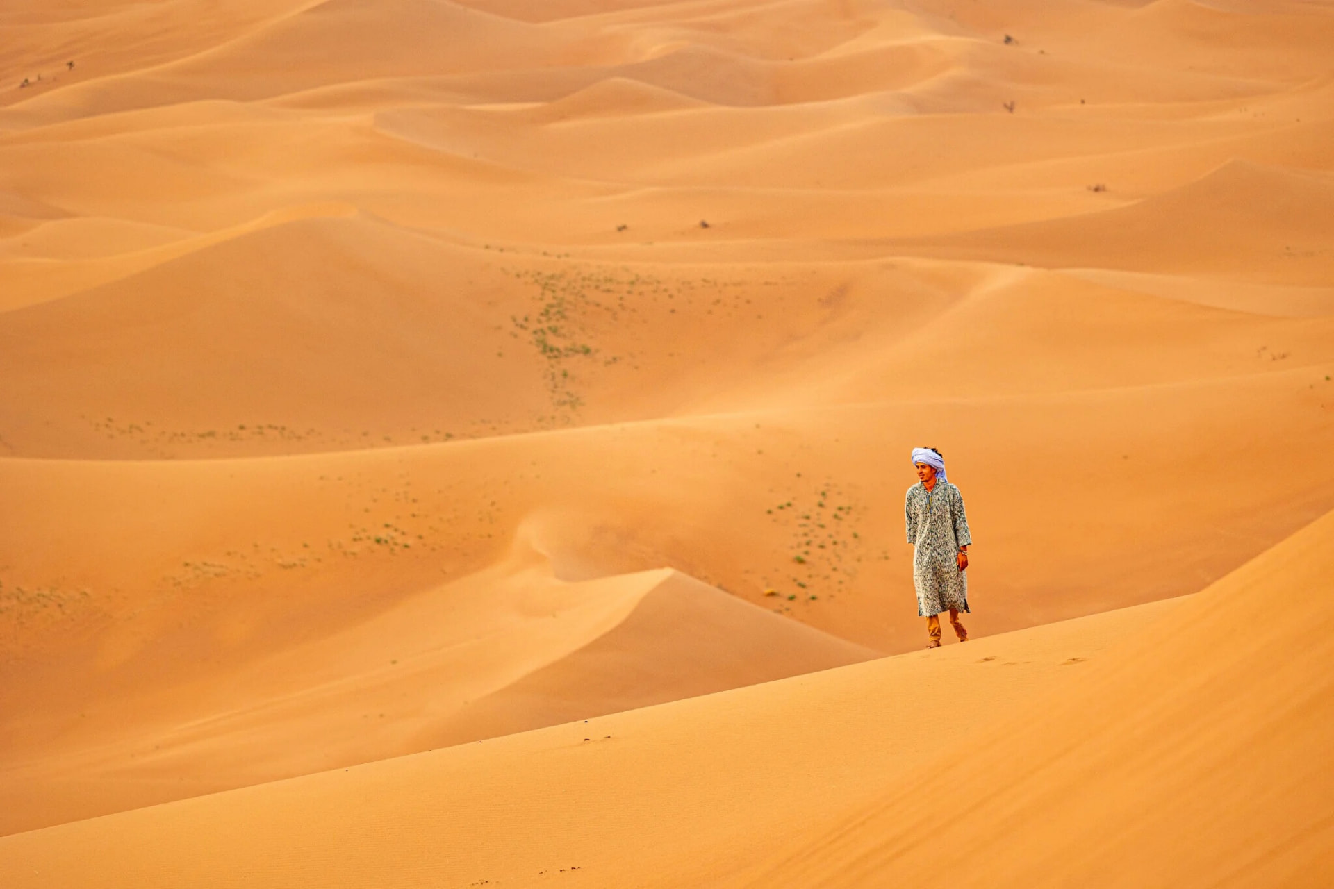 A local guide in a turban walking a dune ridge in the vast Erg Chebbi sand sea