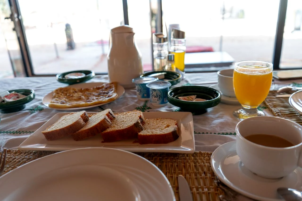 Breakfast table with Moroccan pancakes, cake, orange juice and coffee beside the dining tent windows