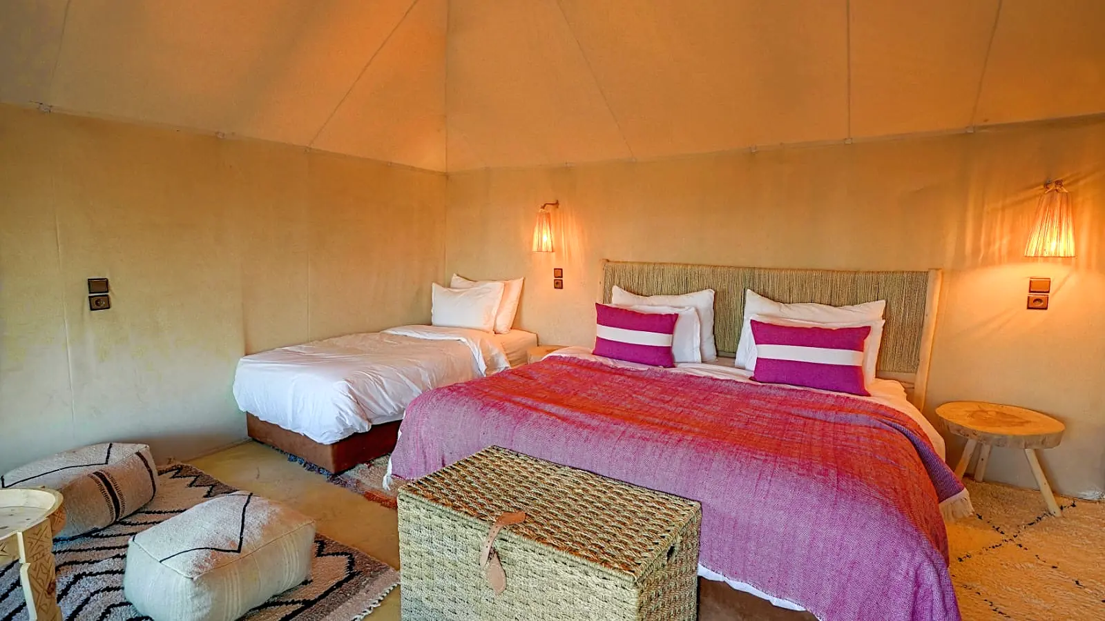 Spacious deluxe tent interior with a large bed, pink and white striped cushions and woven rugs